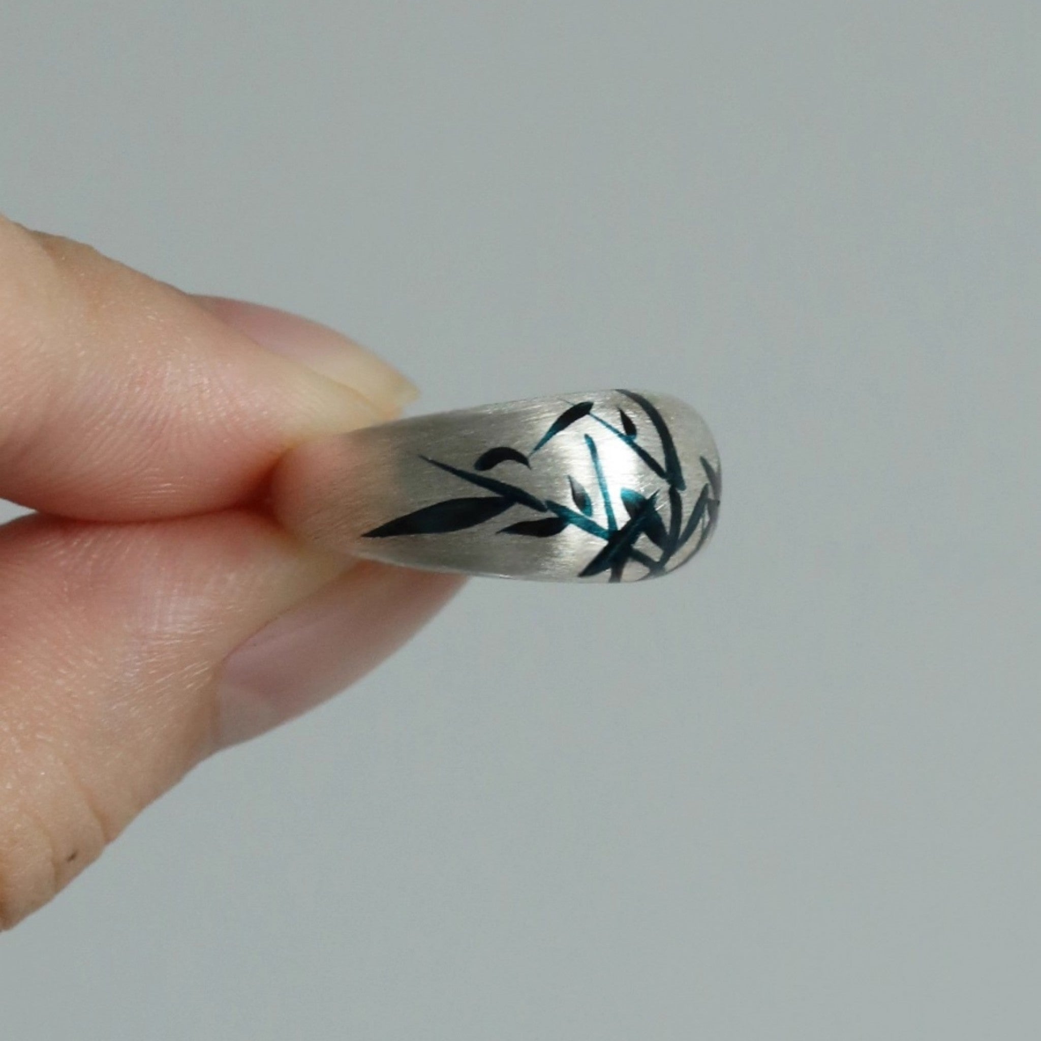 Silver ring with black and green design held by a hand against a gray  LacLume Original Lacquer HandPainted Bamboo Pattern Silver Ringbackground