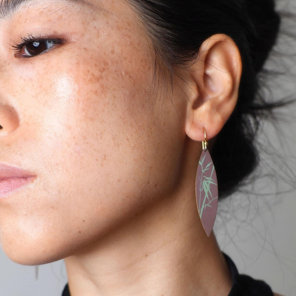 Close-up of a person wearing a leaf-shaped earring with a neutral background