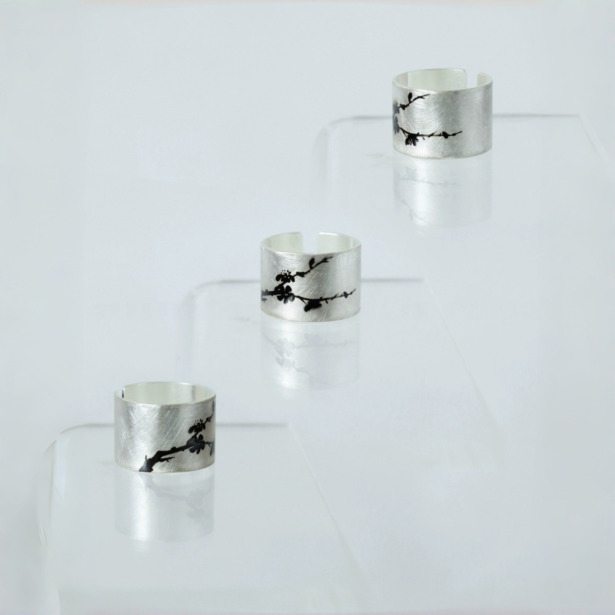 Set of four silver rings with black floral designs on a clear stand against a white background LacLume Handmade Silver Lacquer Ring HandPainted Peach Blossom