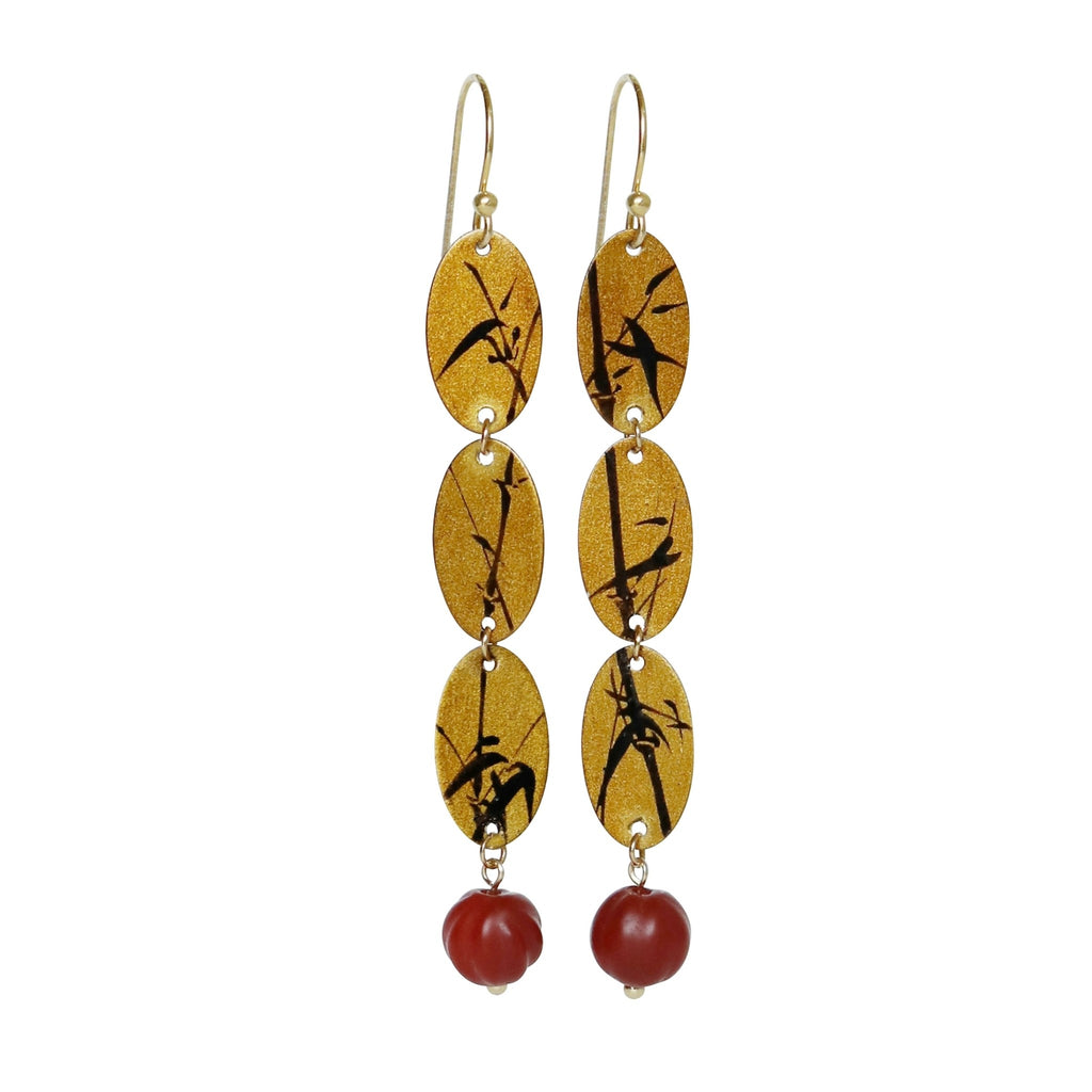 Pair of earrings with gold oval charms and red beads on a white background