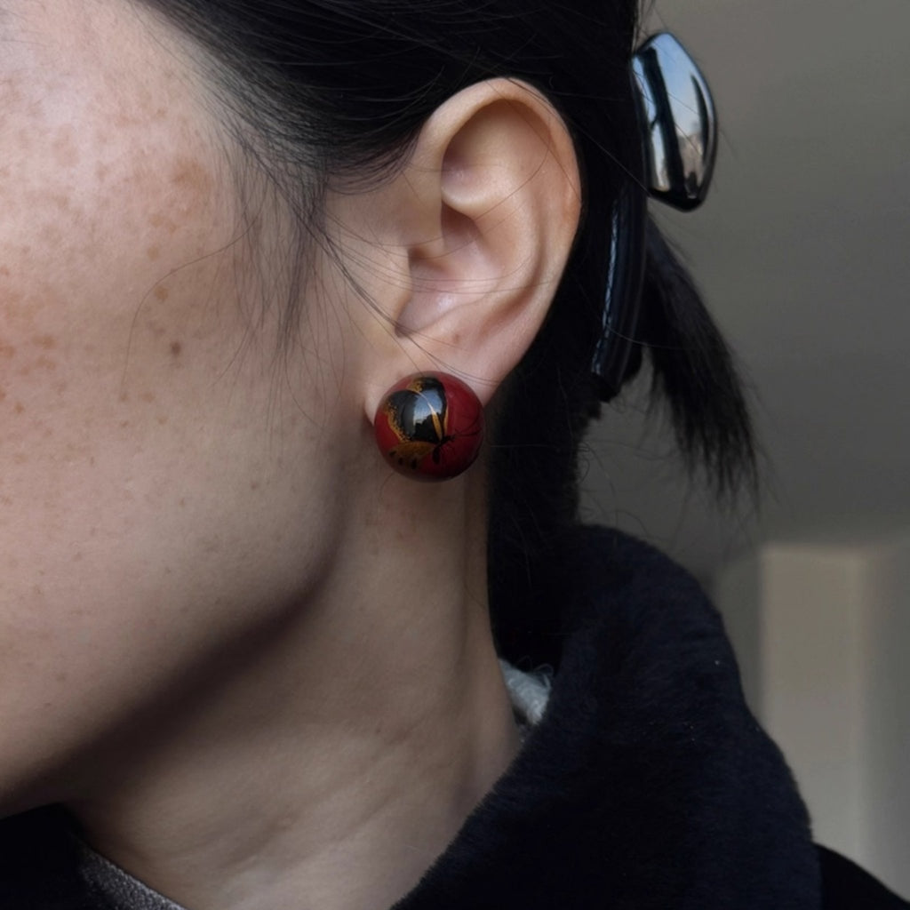 Close-up of a person wearing a red and black earring. LacLume HandPainted Retro Autumn Butterfly Earrings Luxe Artisanal Lacquer Jewelry