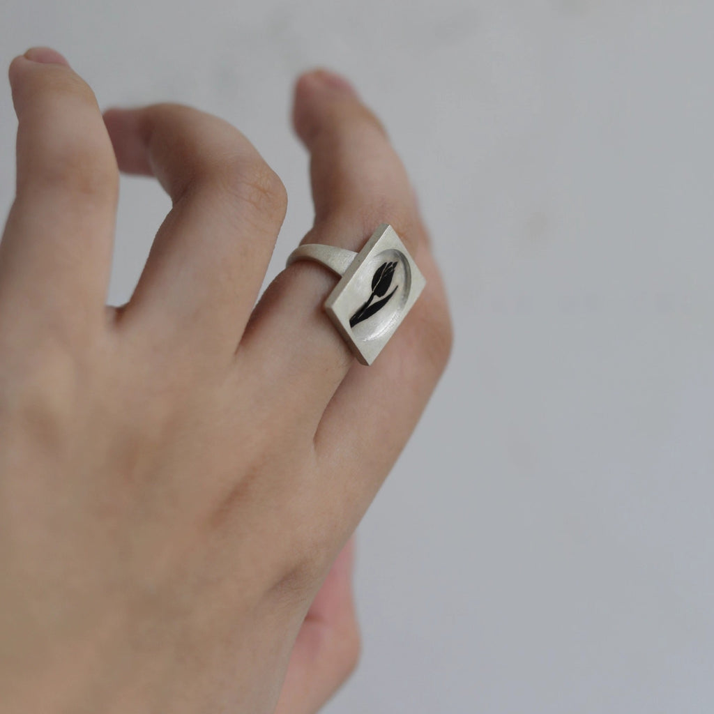 Silver ring with a black design on a person's finger against a plain background