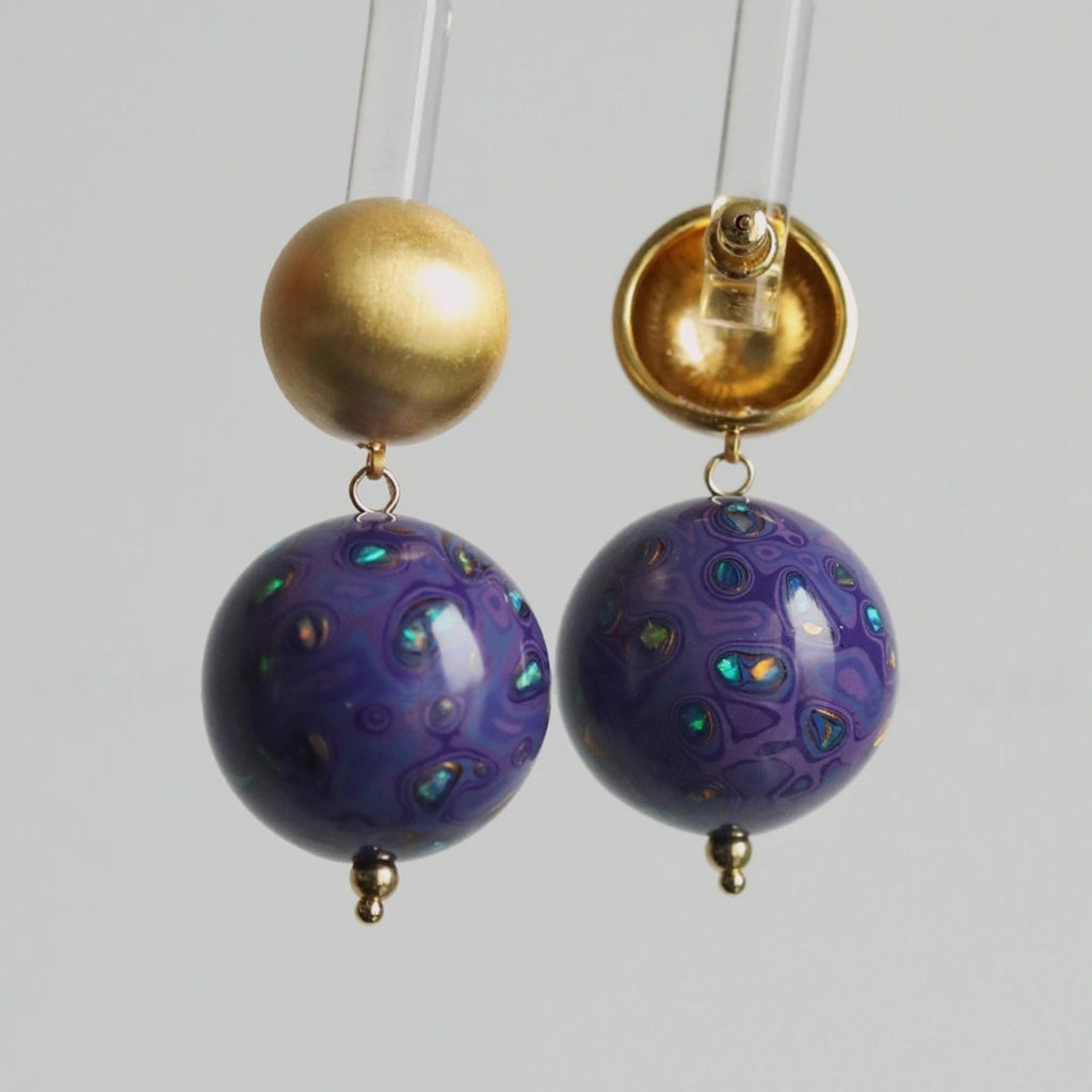 Pair of earrings with gold and purple beads on a light gray background