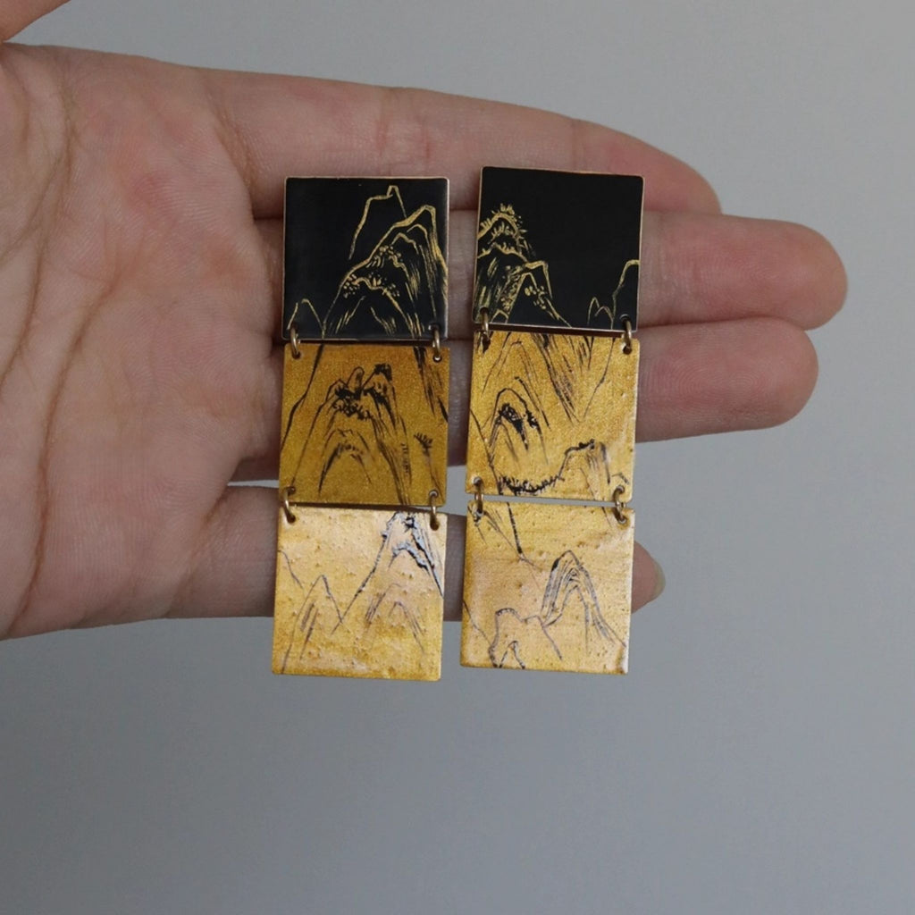 Hand holding a pair of earrings with mountain design