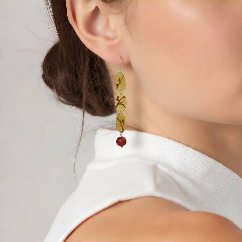 Close-up of a person wearing a pair of earrings with green and red beads on a plain background