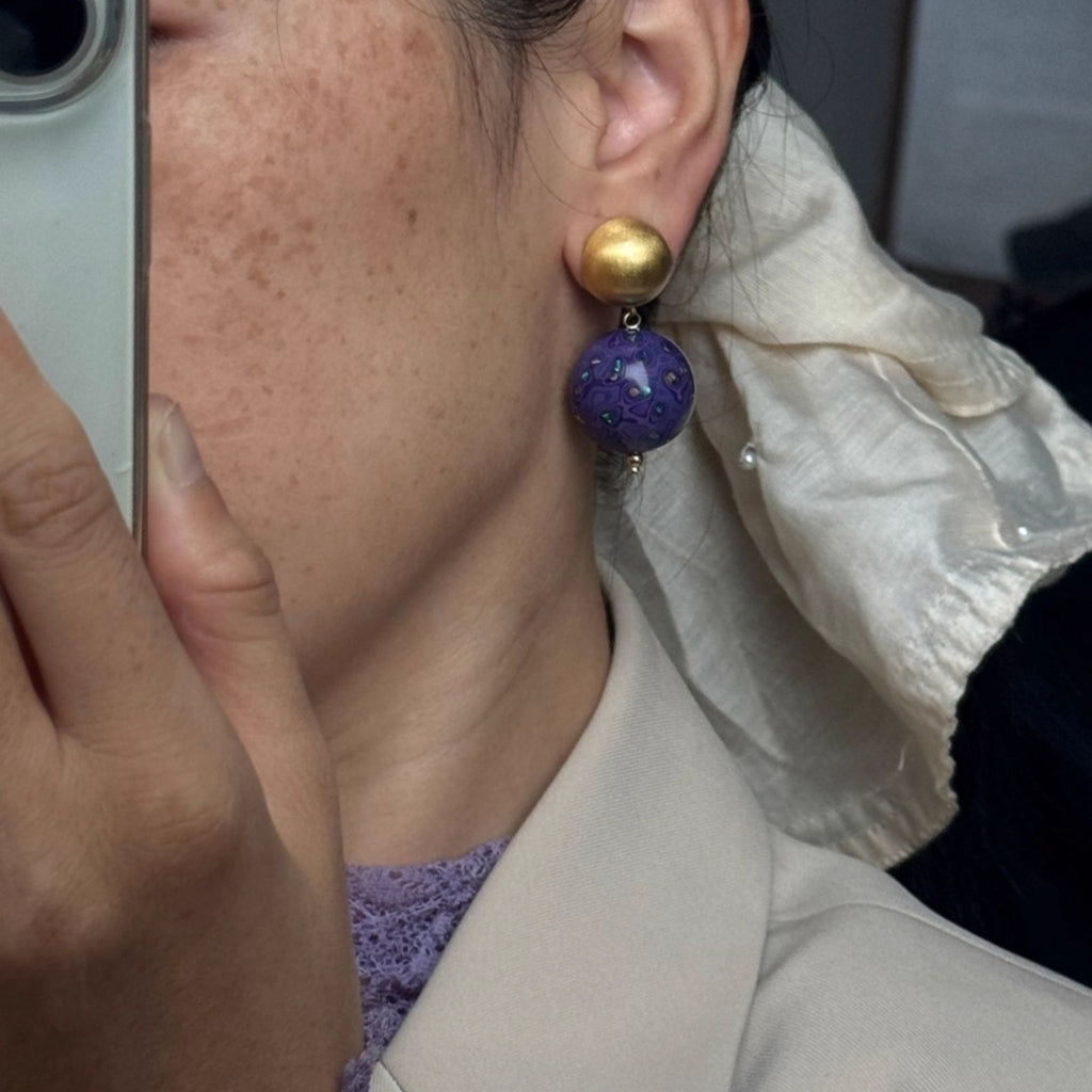 Close-up of a person wearing a gold and purple earring.