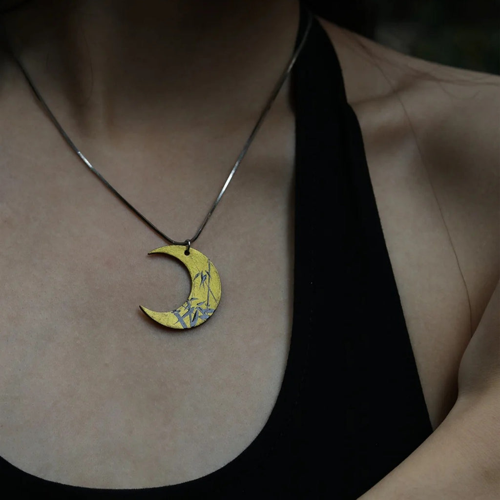 Person wearing a necklace with a crescent moon pendant featuring bamboo design.