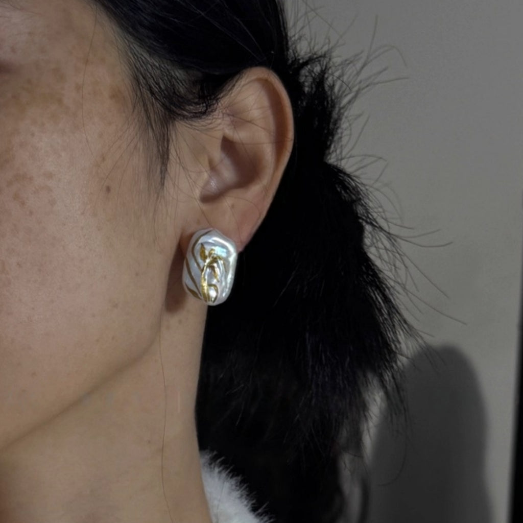 Close-up of an ear wearing a gold and silver earring against a neutral background