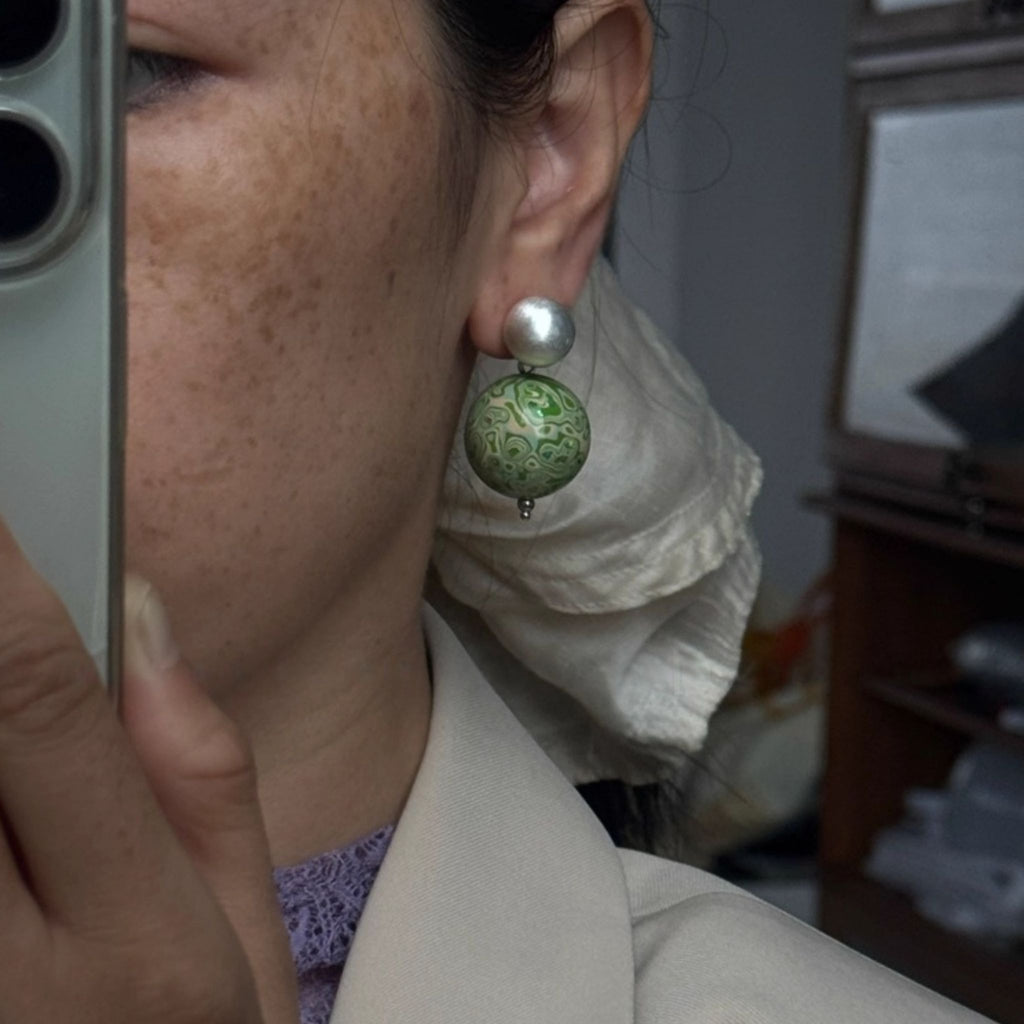 Close-up of a person wearing a green and silver earring indoors.